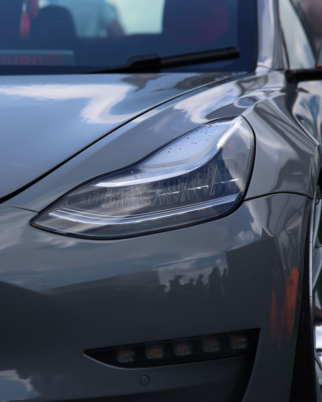 A person wearing black gloves is polishing a black car