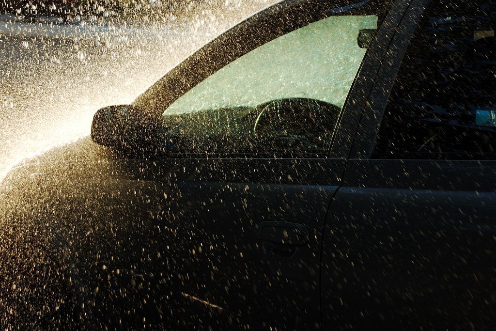 A car being sprayed with water illustrates the hydrophobic effect and environmental protection provided by ceramic coating. The water beads and flows off the car’s surface, enhancing cleanliness and minimizing buildup.