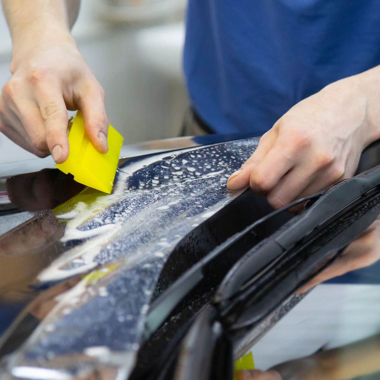A person is cleaning a blue car with an orange towel