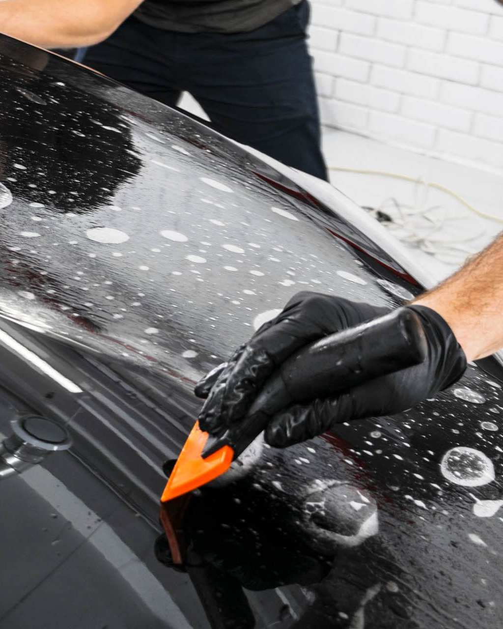 A person wearing black gloves is polishing a black car