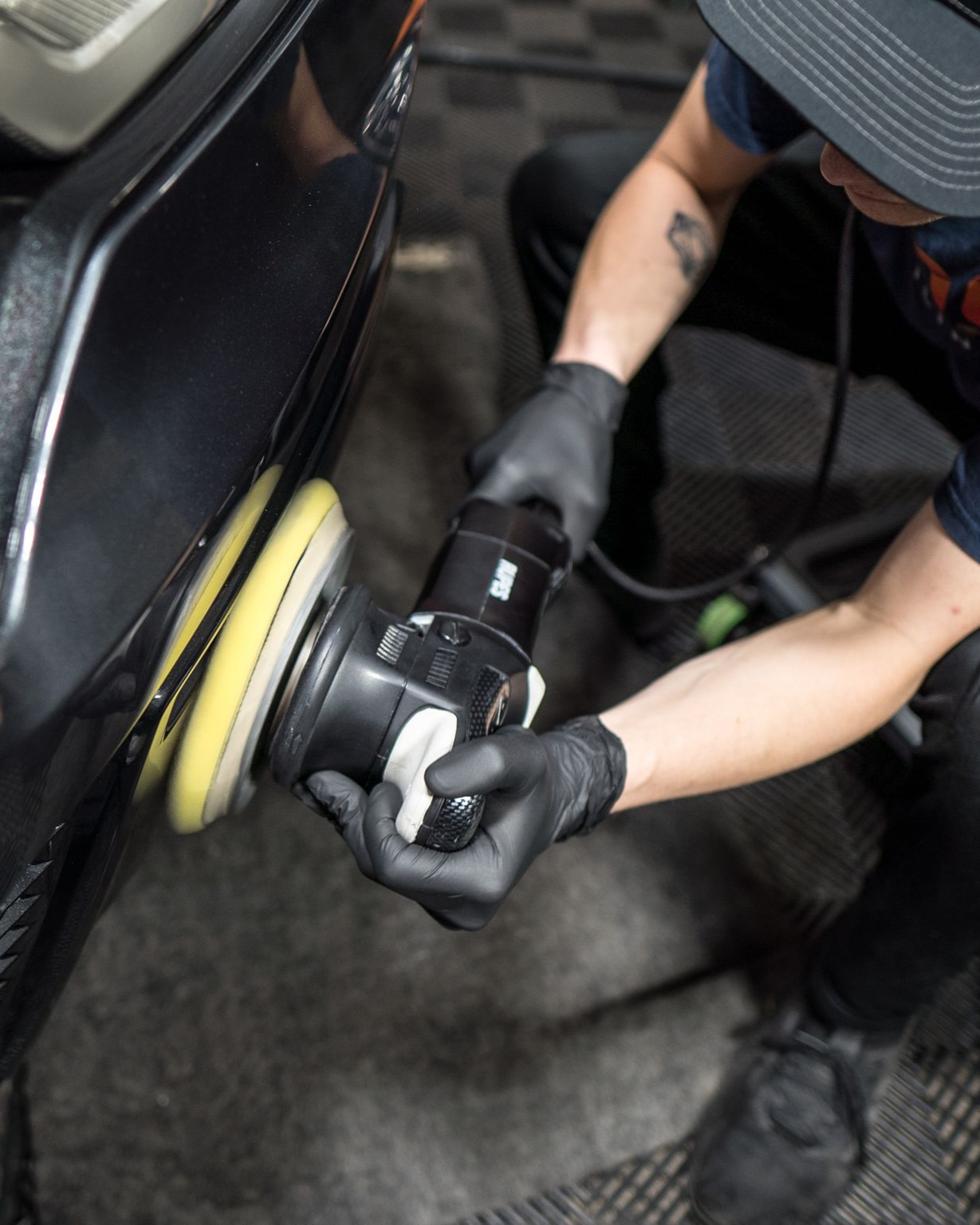 A person wearing black gloves is polishing a black car