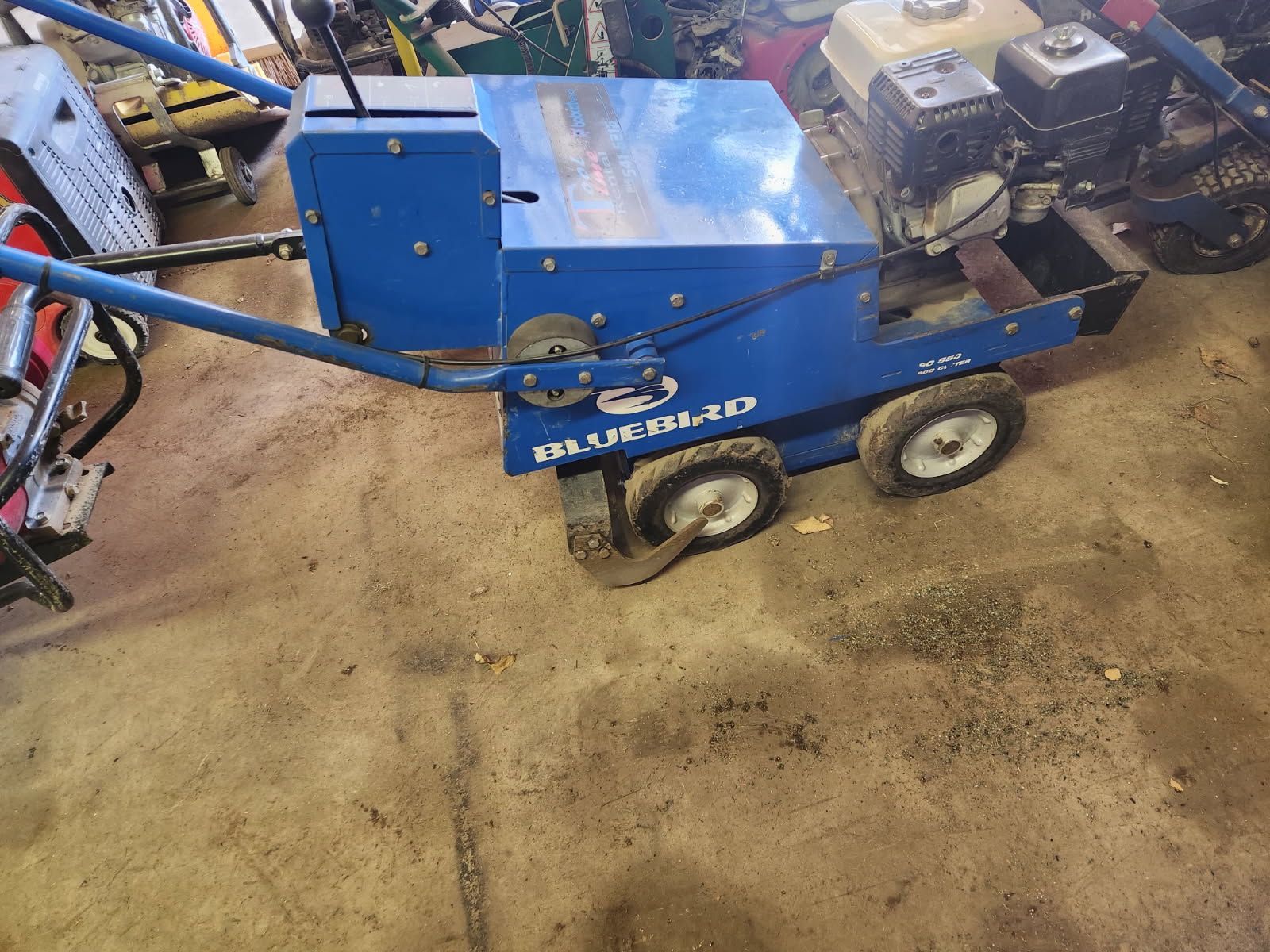 Blue industrial machine with two wheels in a workshop, surrounded by tools and equipment.