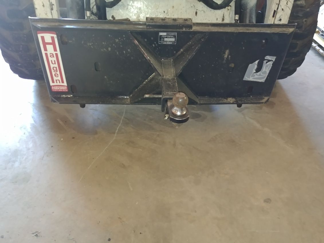 Black trailer hitch on concrete floor in front of a metal trailer bumper with warning decals