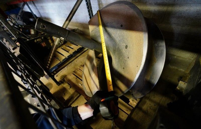 Person measuring a large circular metal part in an industrial workshop with a yellow tape measure