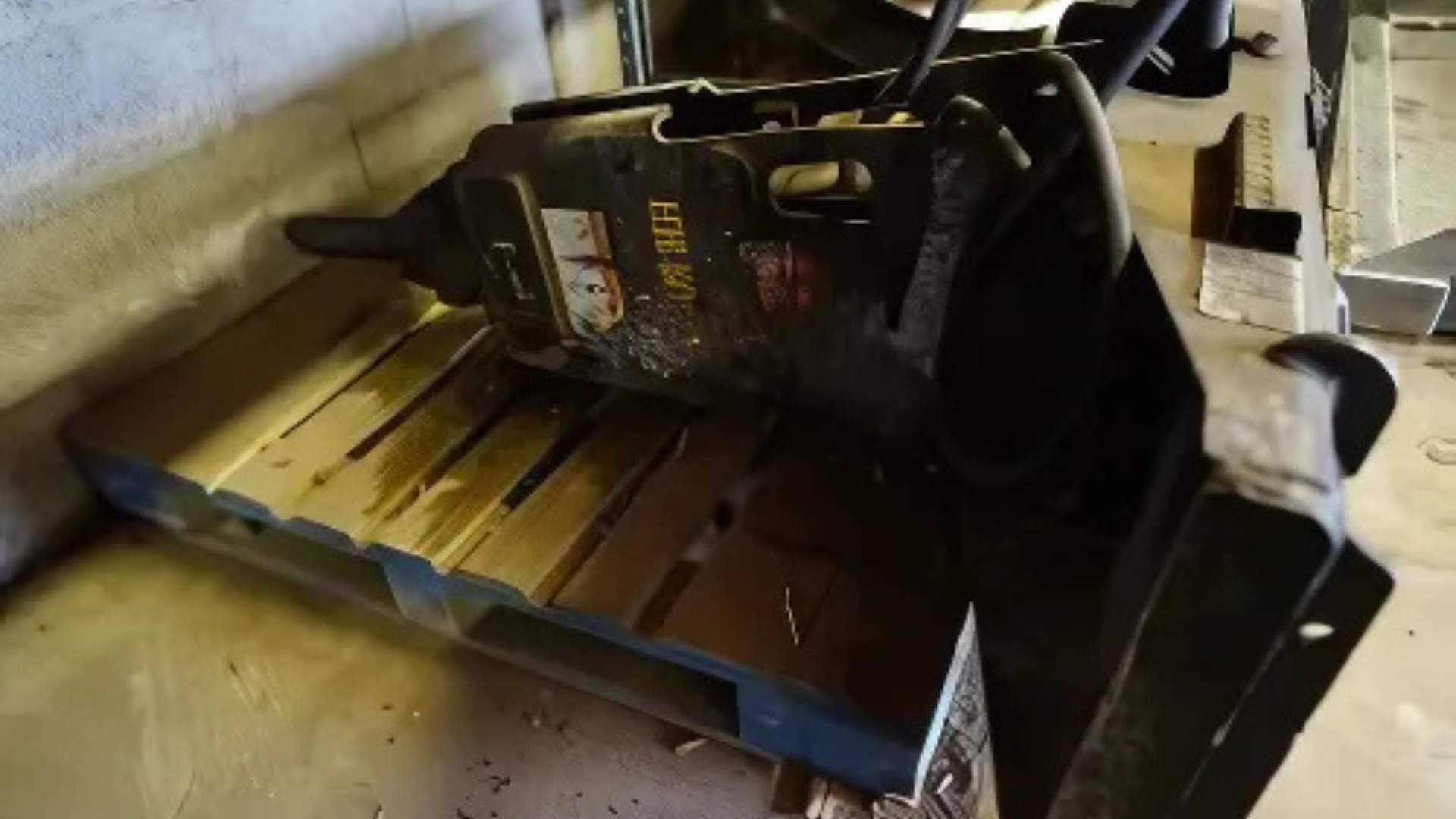 A chainsaw lying on a wooden bench indoors, with a black fuel tank and metal blade