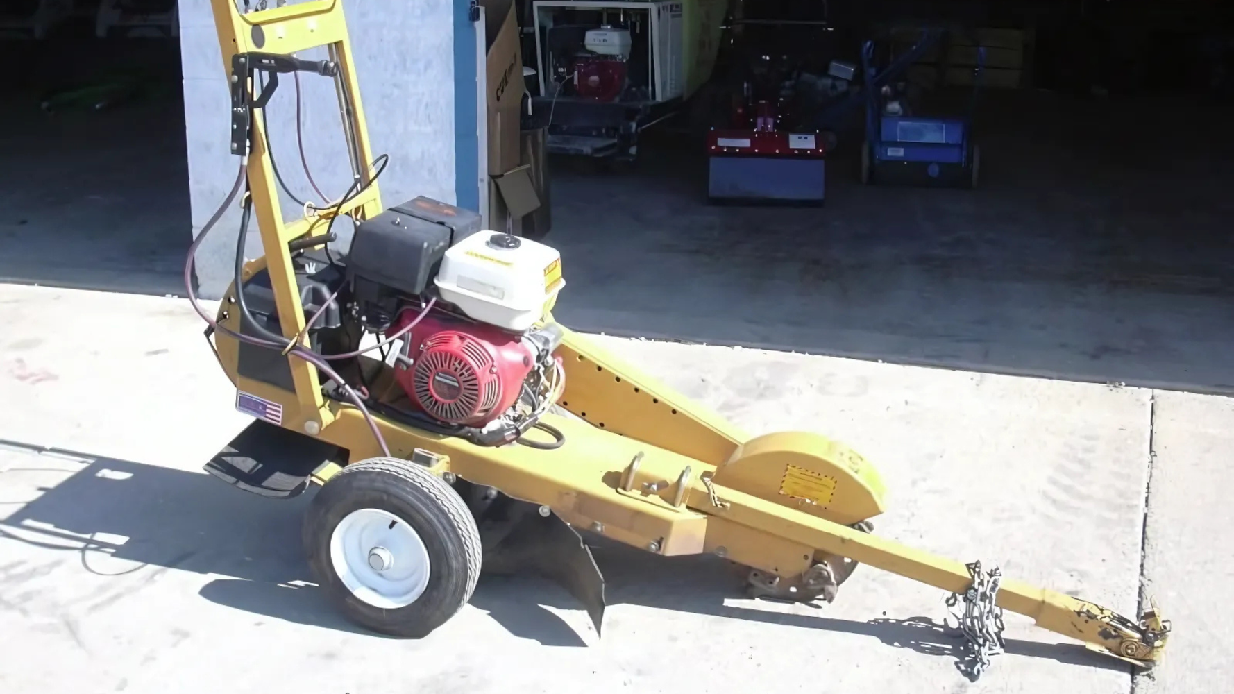 Yellow tow-behind mower with red engine parked in a garage driveway.