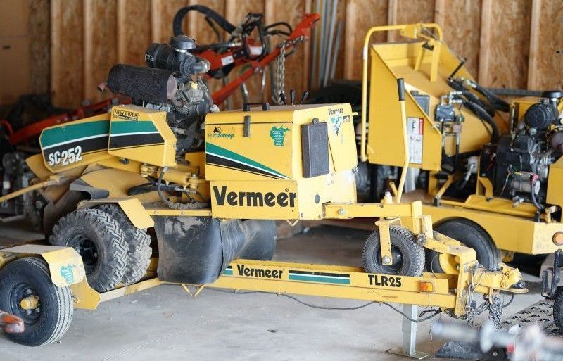 Yellow Vermeer road grader parked in a garage, with black tires and attached machinery.