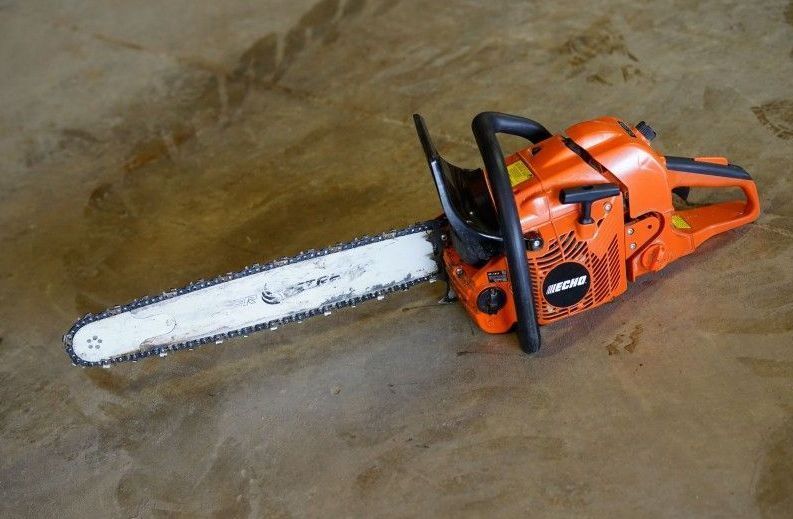 Orange chainsaw lying on a concrete floor with a white saw blade