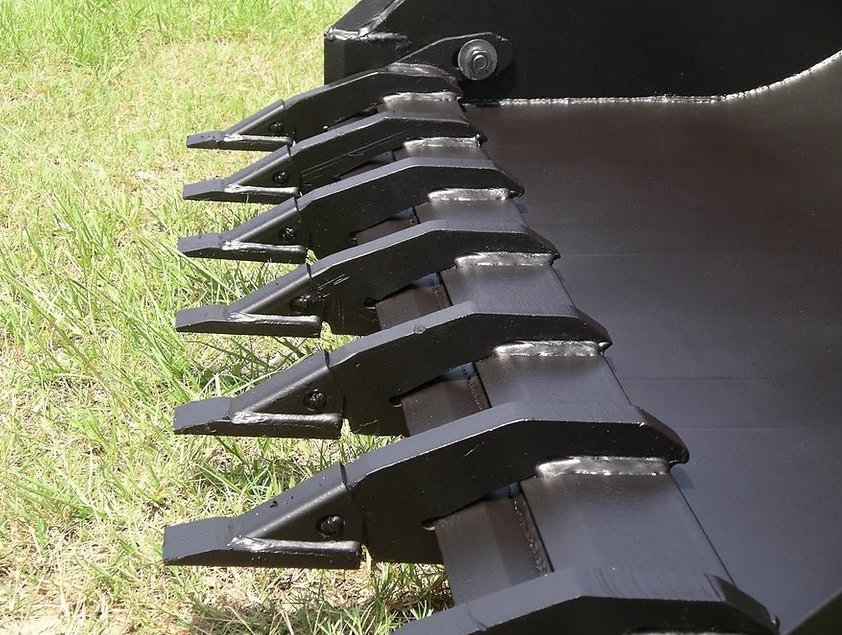 Close-up of black metal excavator bucket teeth against grass