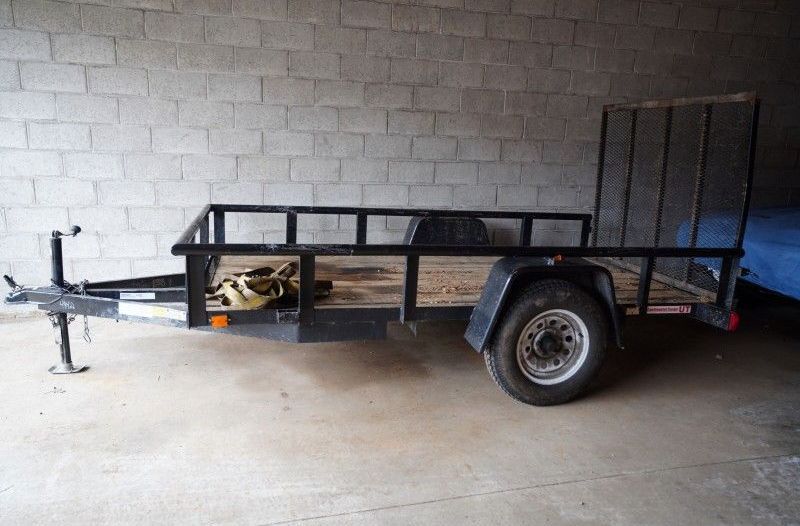 Black flatbed utility trailer parked indoors against a cinderblock wall.