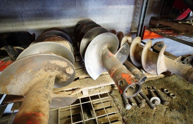 Rusty industrial auger screws lined up in a dusty metal storage area