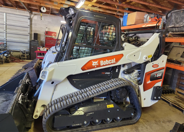 Bobcat compact track loader with a white cab and orange panel inside a workshop garage.