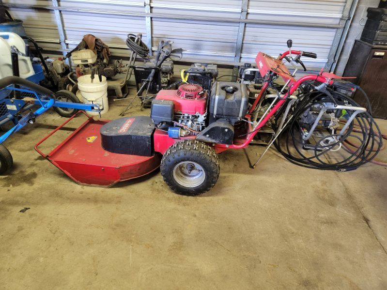 Red walk-behind mower/tractor in a cluttered workshop, with tools and equipment in the background
