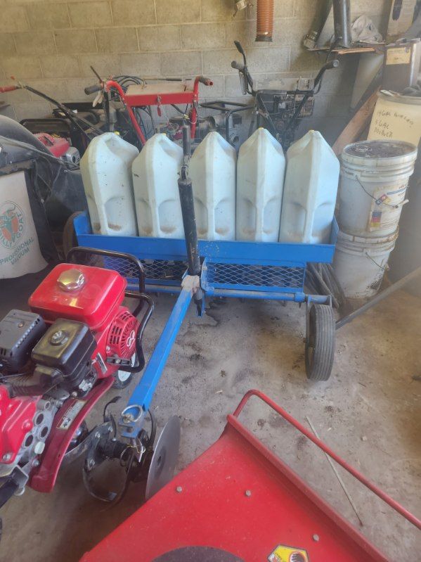 Blue utility trailer with white containers in a garage, beside a red motorized machine.