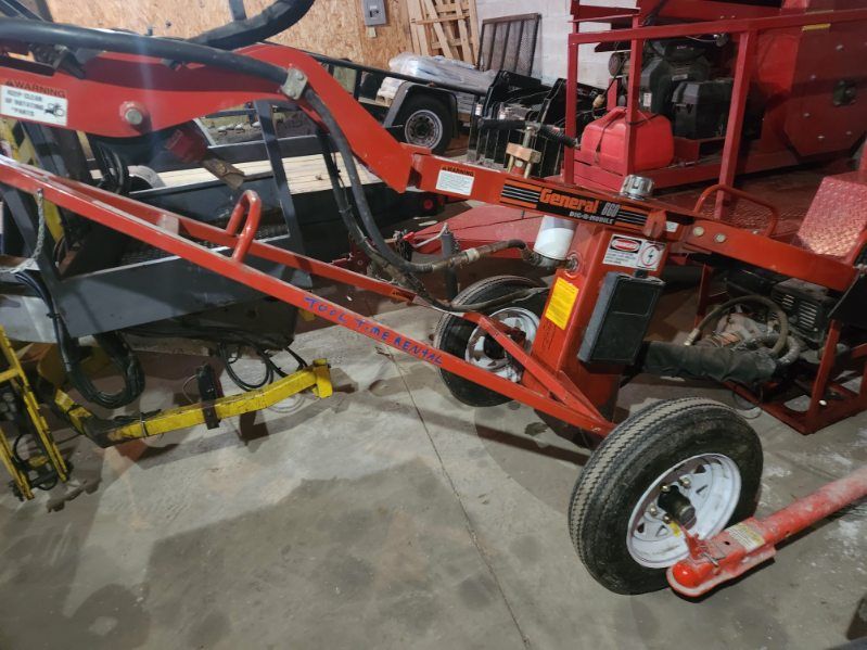 Red farm machinery with a wheel, frame, and attached yellow implement in a workshop.