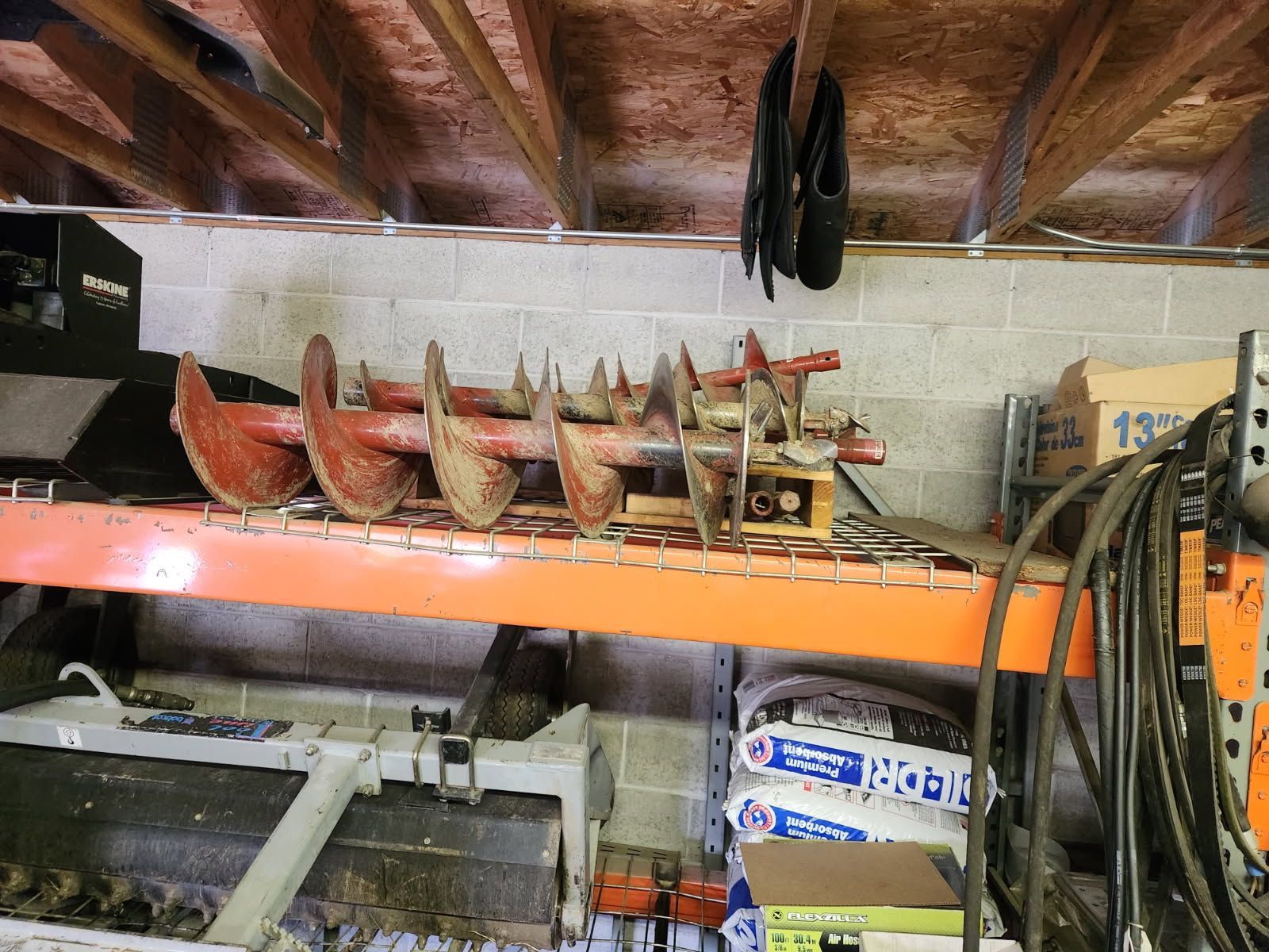 Storage shelf with rows of rusty metal auger bits, hoses, and boxes in a workshop garage