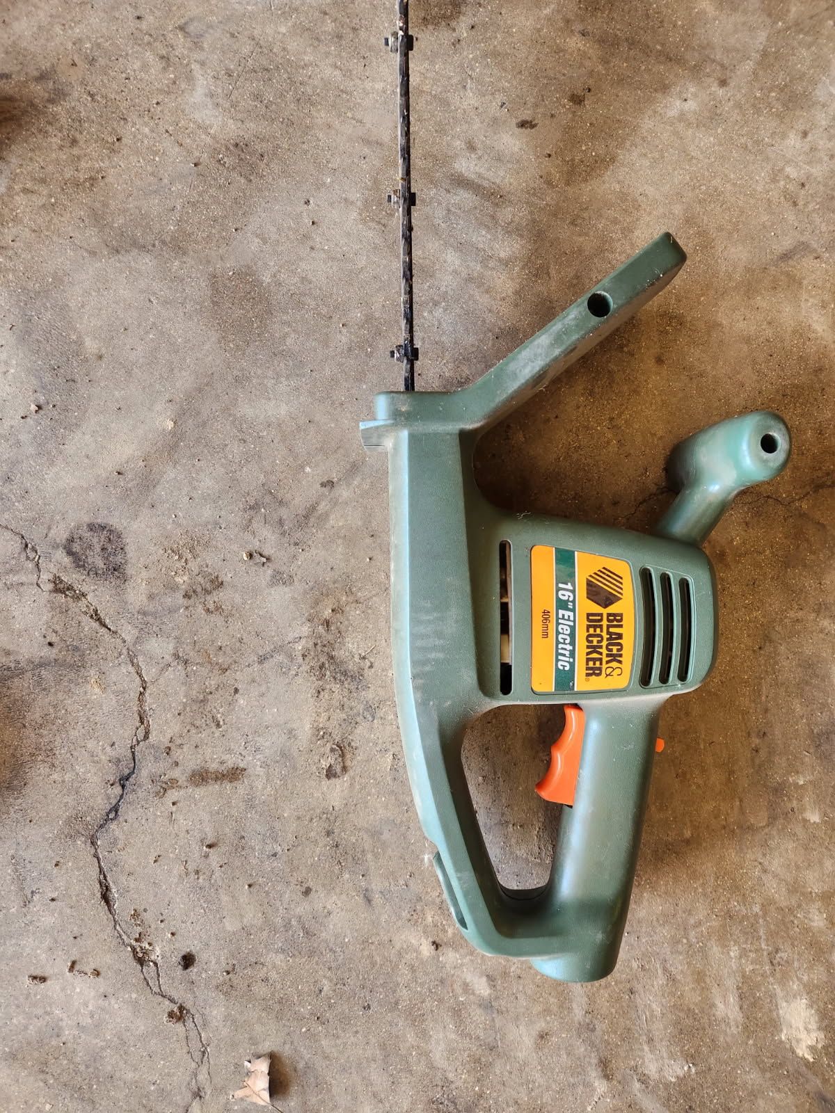 Green and orange electric jigsaw with cord, lying on a concrete floor рядом with a small drill bit