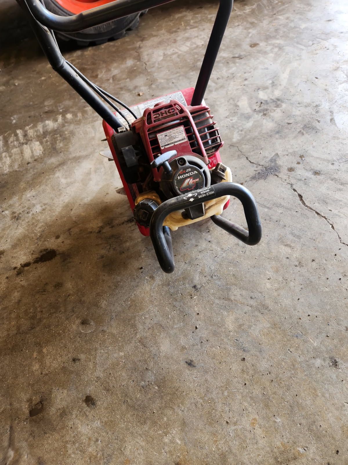 Red and black lawn edger on a concrete floor, with handlebars and a front guard visible.