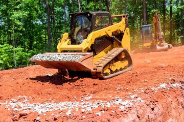 Yellow bulldozer grading red dirt on a forested construction site