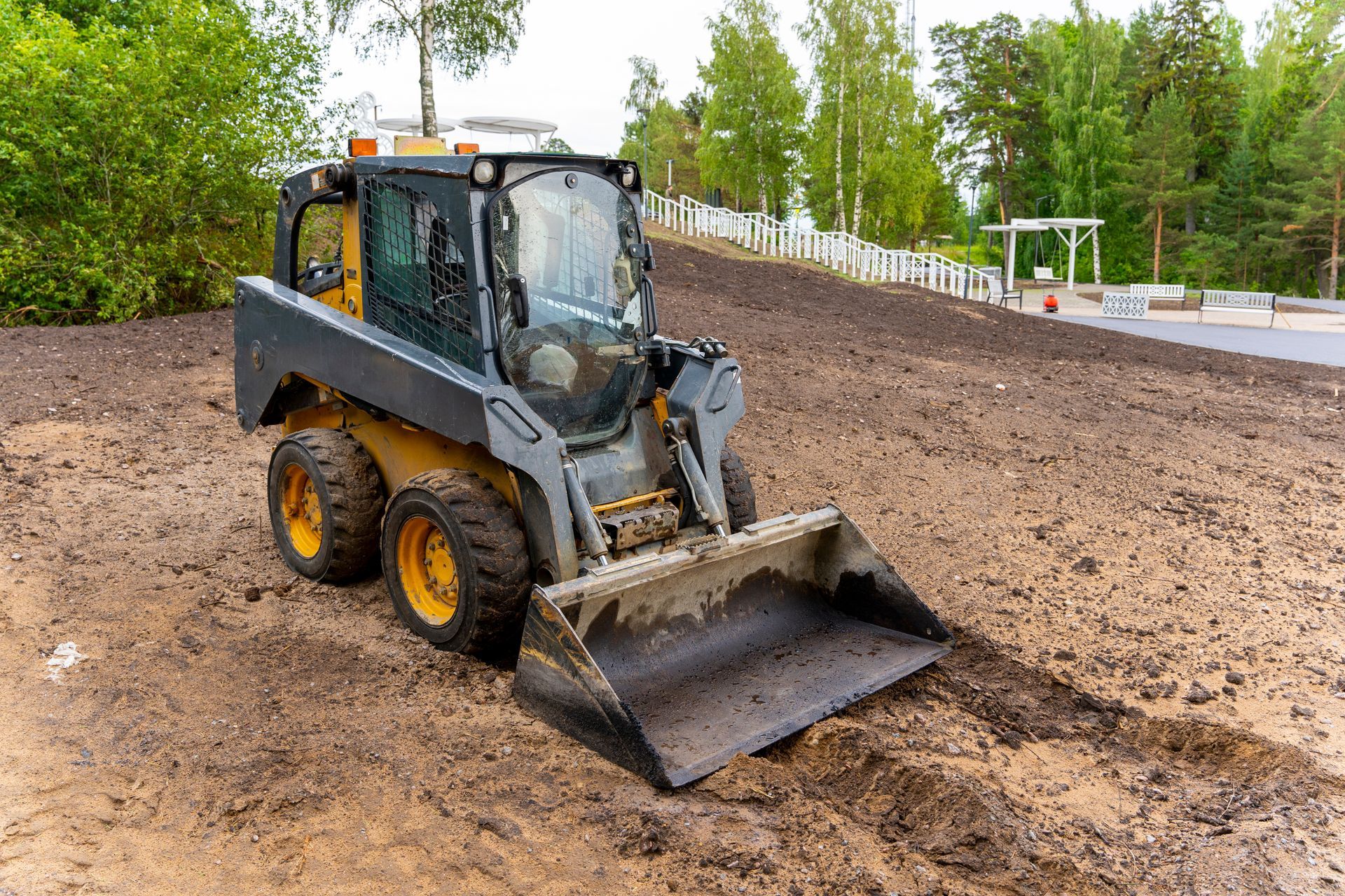 Small skid steer loader on a muddy construction site with trees in the background