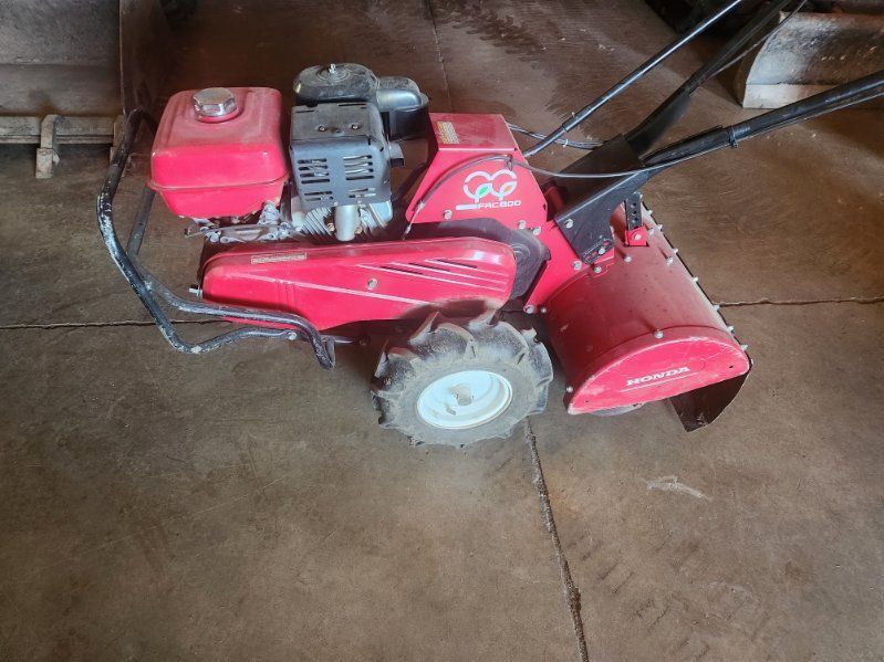 Red snow blower with black handle and white wheel on a concrete floor