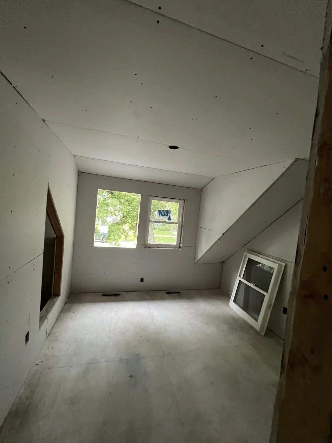 Unfinished room with drywall and windows. A window screen leans against a wall.