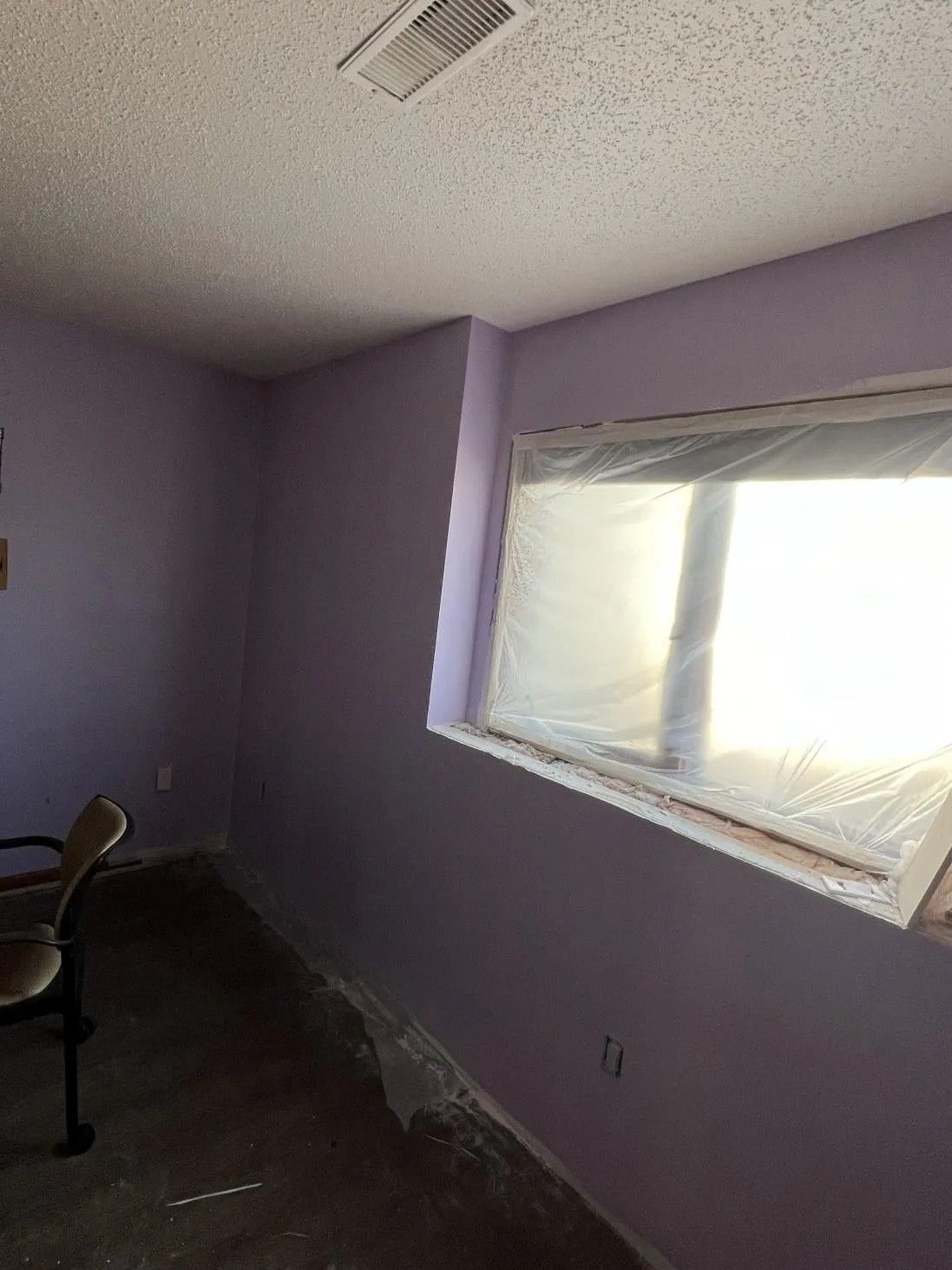 Interior of a room painted lavender, with a window covered in plastic sheeting.