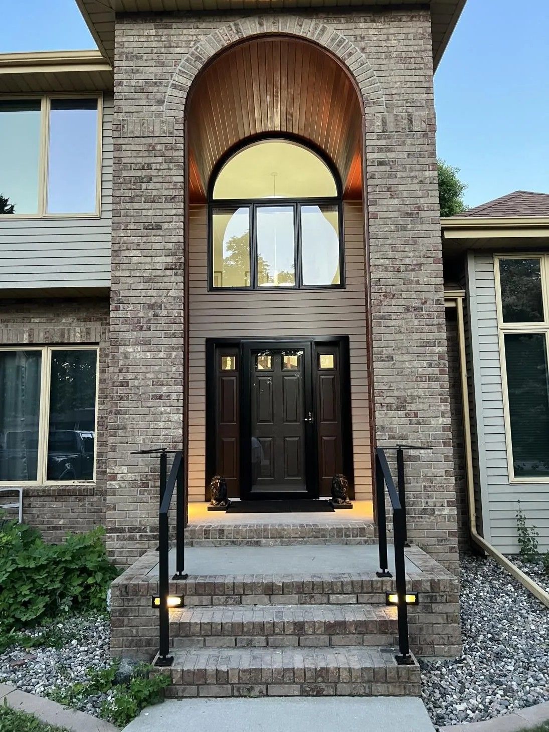 Brick facade entrance with arched top, dark wood door, steps with handrails, and a large window.