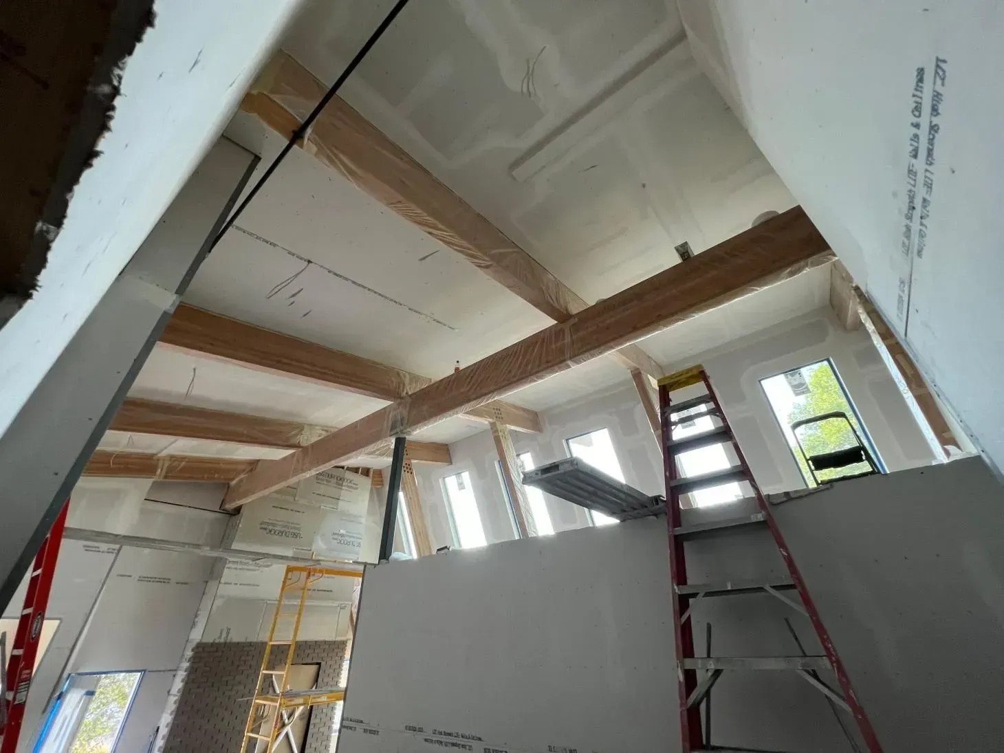 Interior of a building under construction. Visible are exposed wooden beams, drywall, and a ladder.