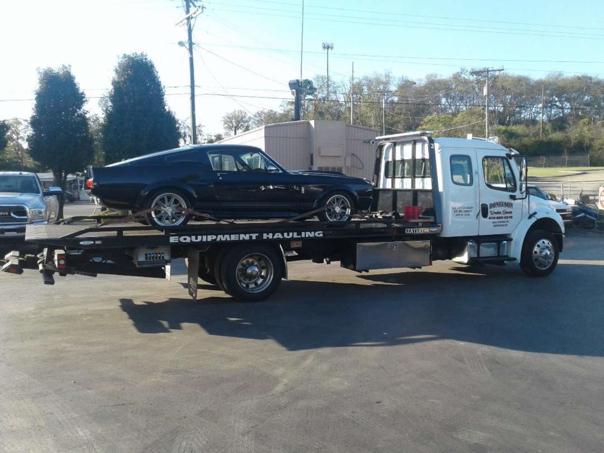 Black classic car on a flatbed tow truck. Sunny outdoor setting. 