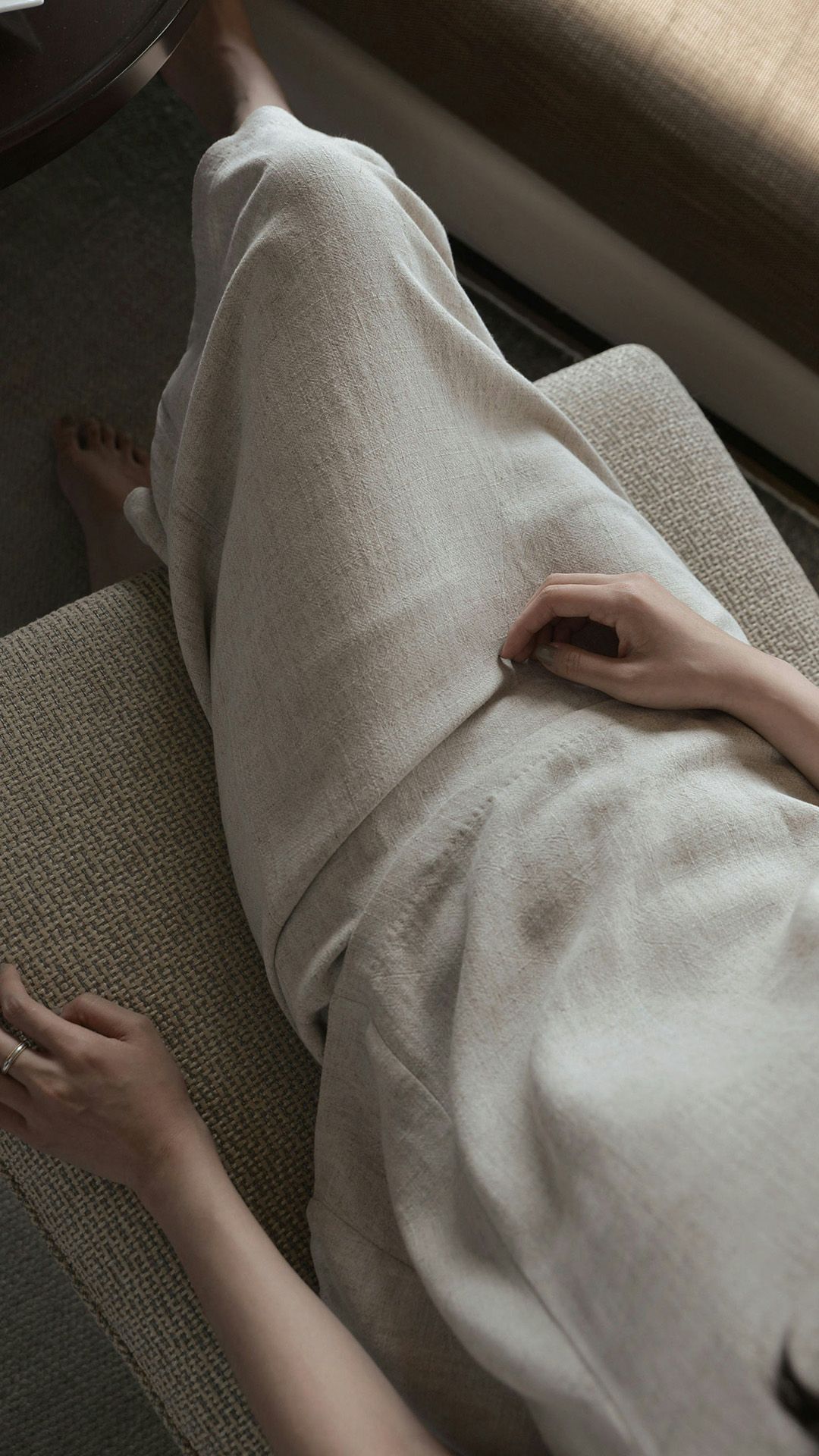 Person wearing a light-colored robe relaxing on a cushioned surface. Hands are resting.