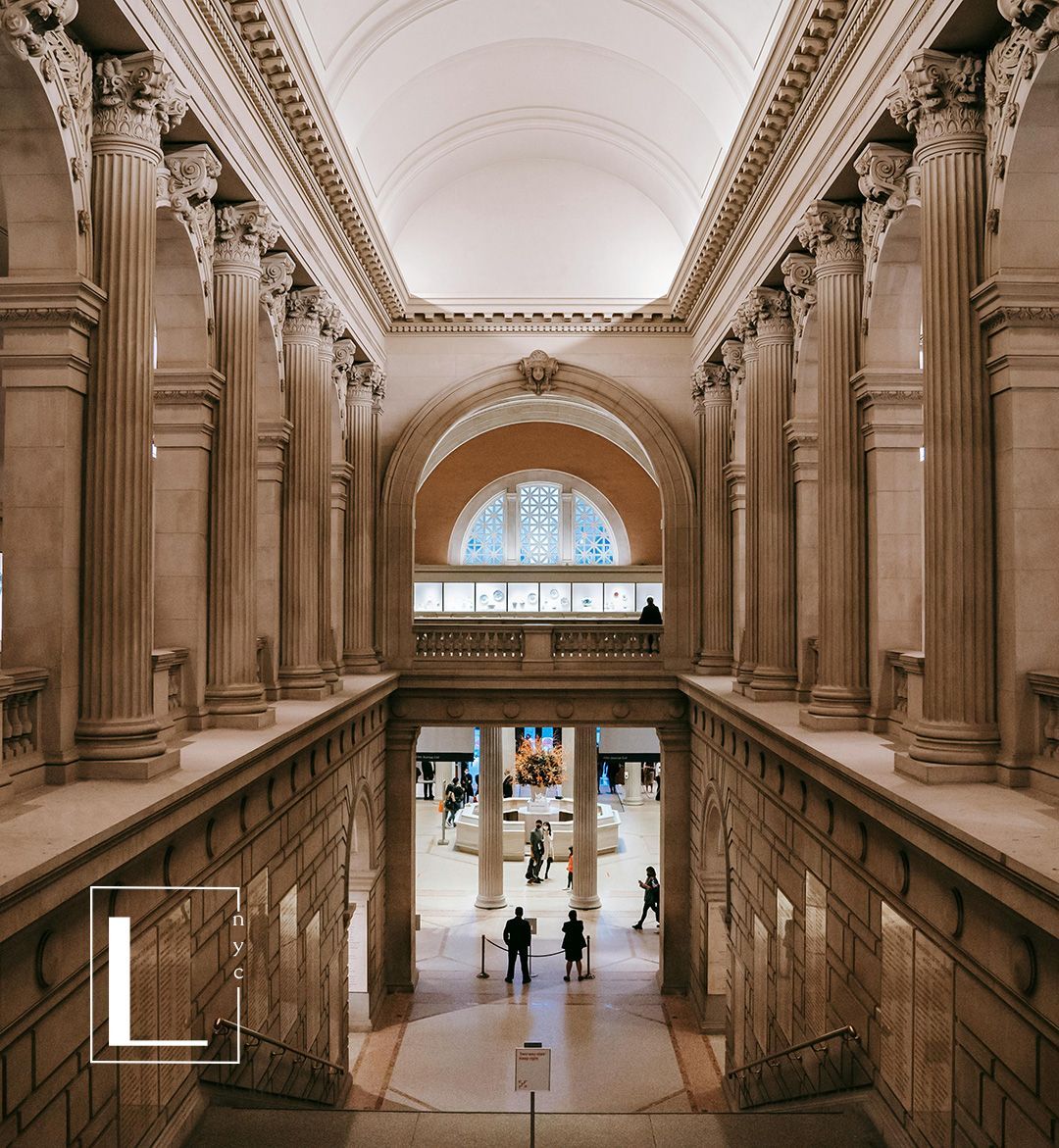 Grand hall in a museum, with columns, arched ceilings, and people walking below. Beige and white tones.