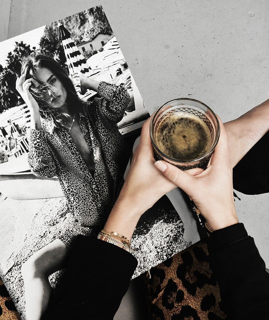 Person holding a coffee in a clear glass, with a black and white magazine spread in the background.