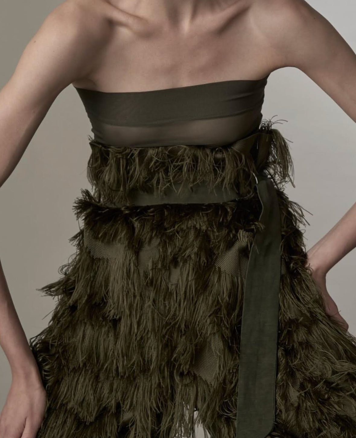 Woman in olive green strapless dress with fringe detail and a sash.