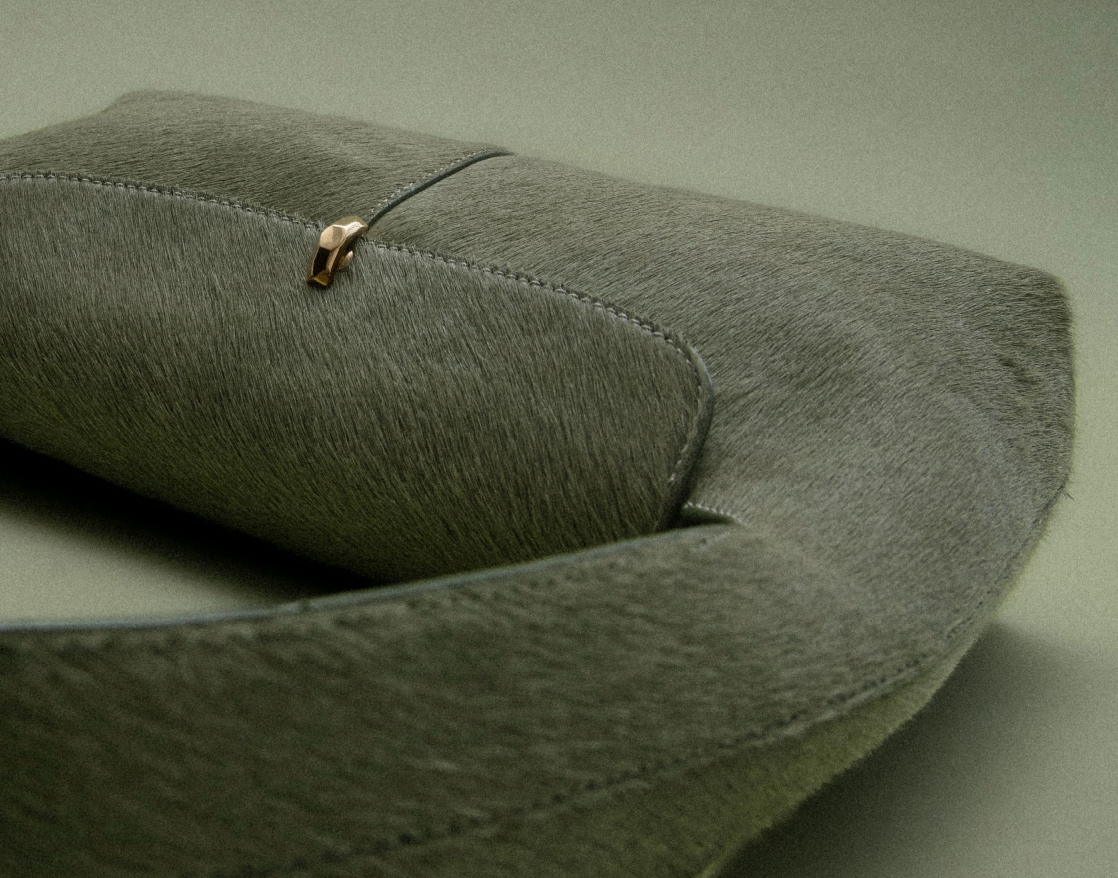 Close-up of a rolled-up, olive-green suede strap with a small gold-toned clasp.