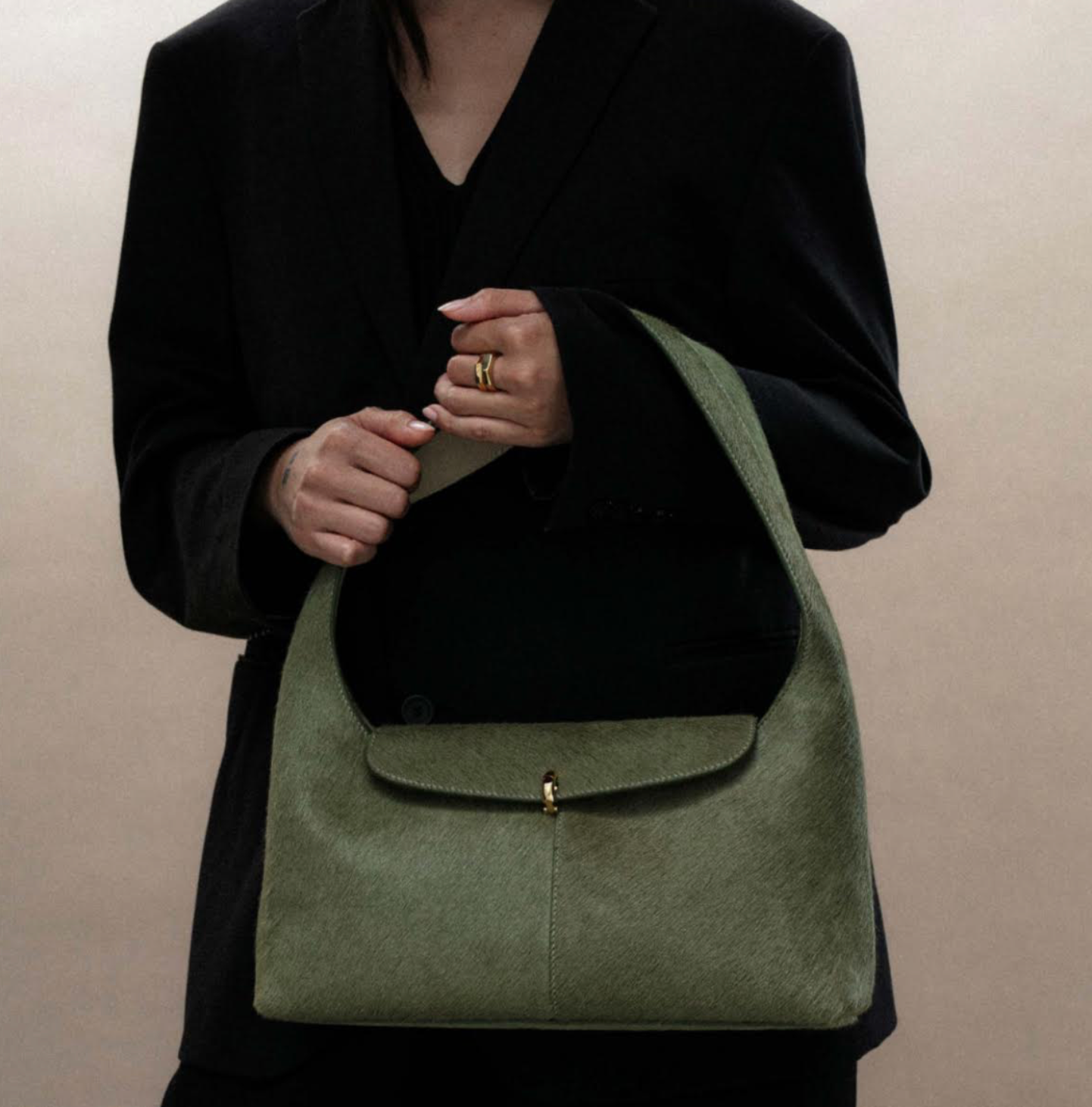 Woman in black blazer holds a green shoulder bag with a flap closure.