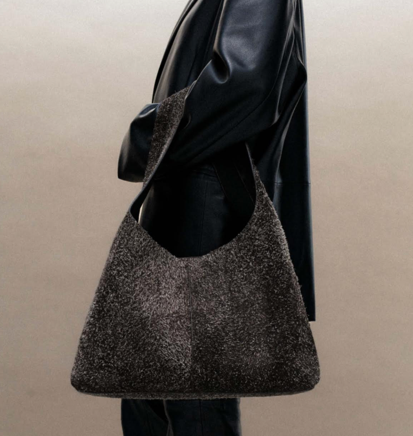 Person wearing a sparkly, dark-colored hobo bag over a black leather jacket.
