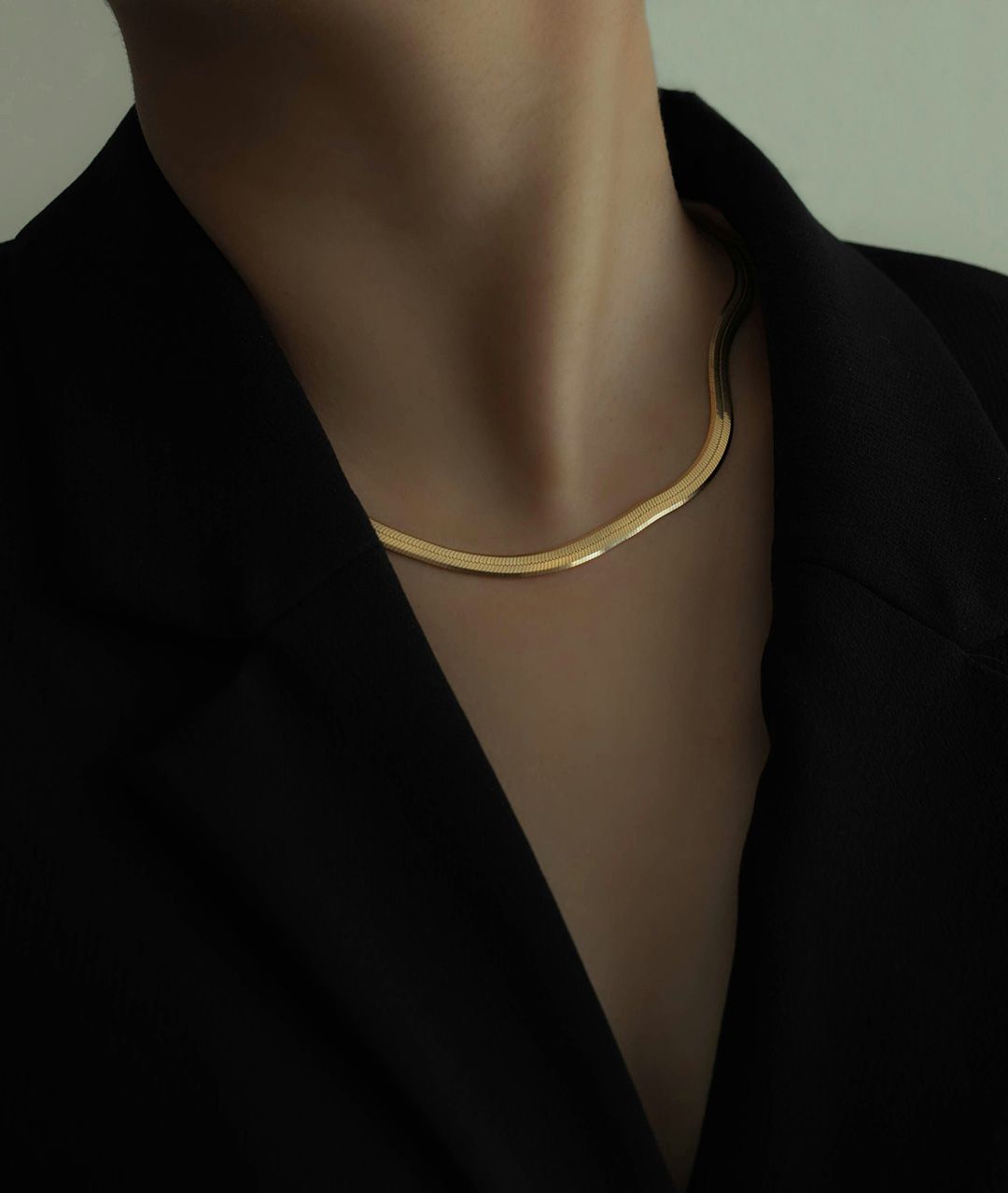 Gold herringbone necklace on a person wearing a black blazer.
