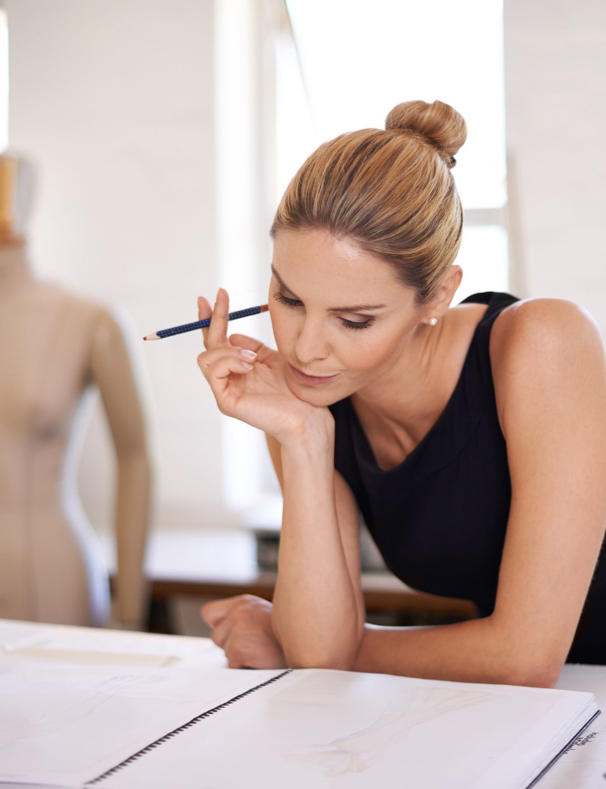 Woman with a pencil in her hand looking at a drawing; a mannequin in the background.
