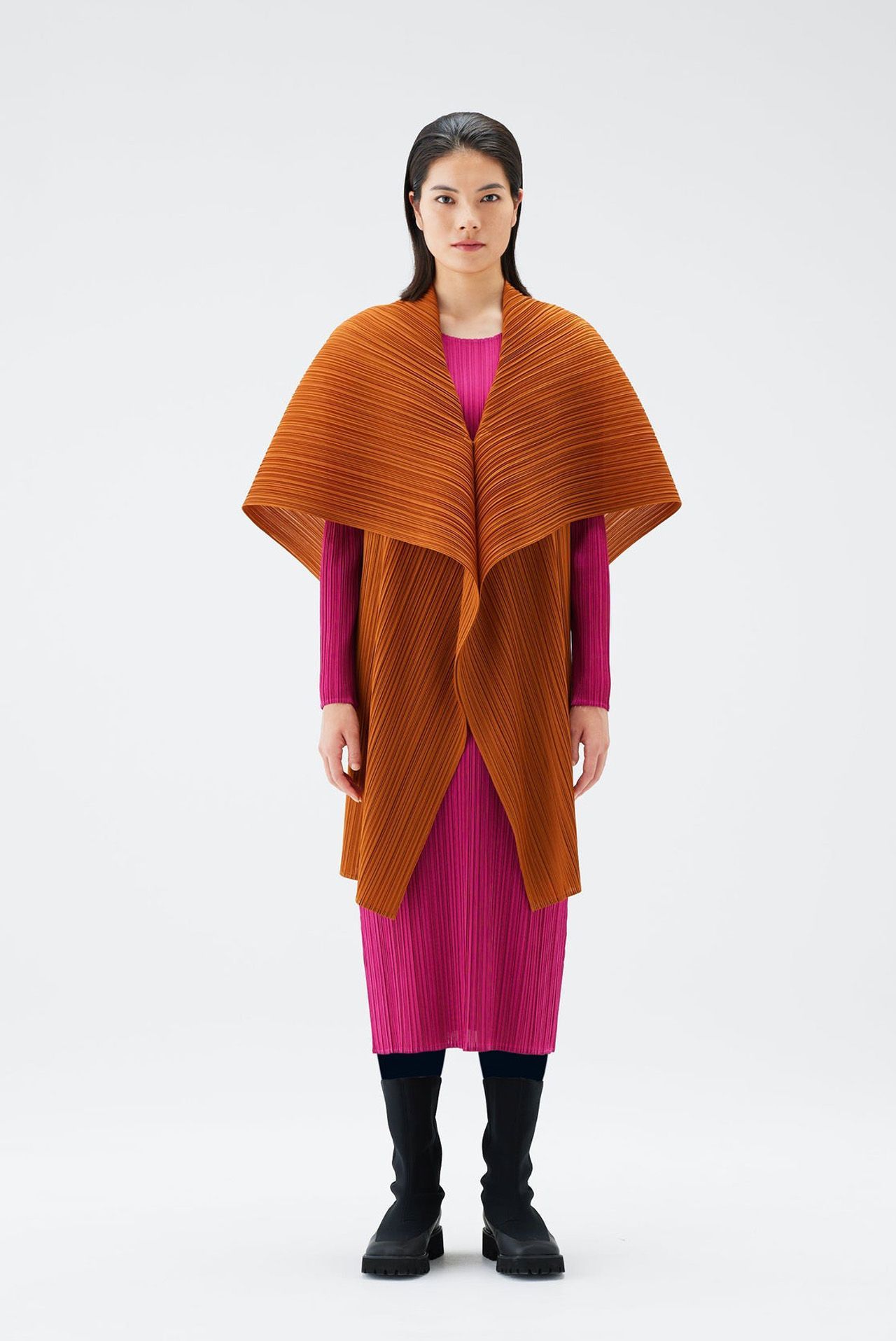 Woman in pink dress and orange textured cape, standing on white background.