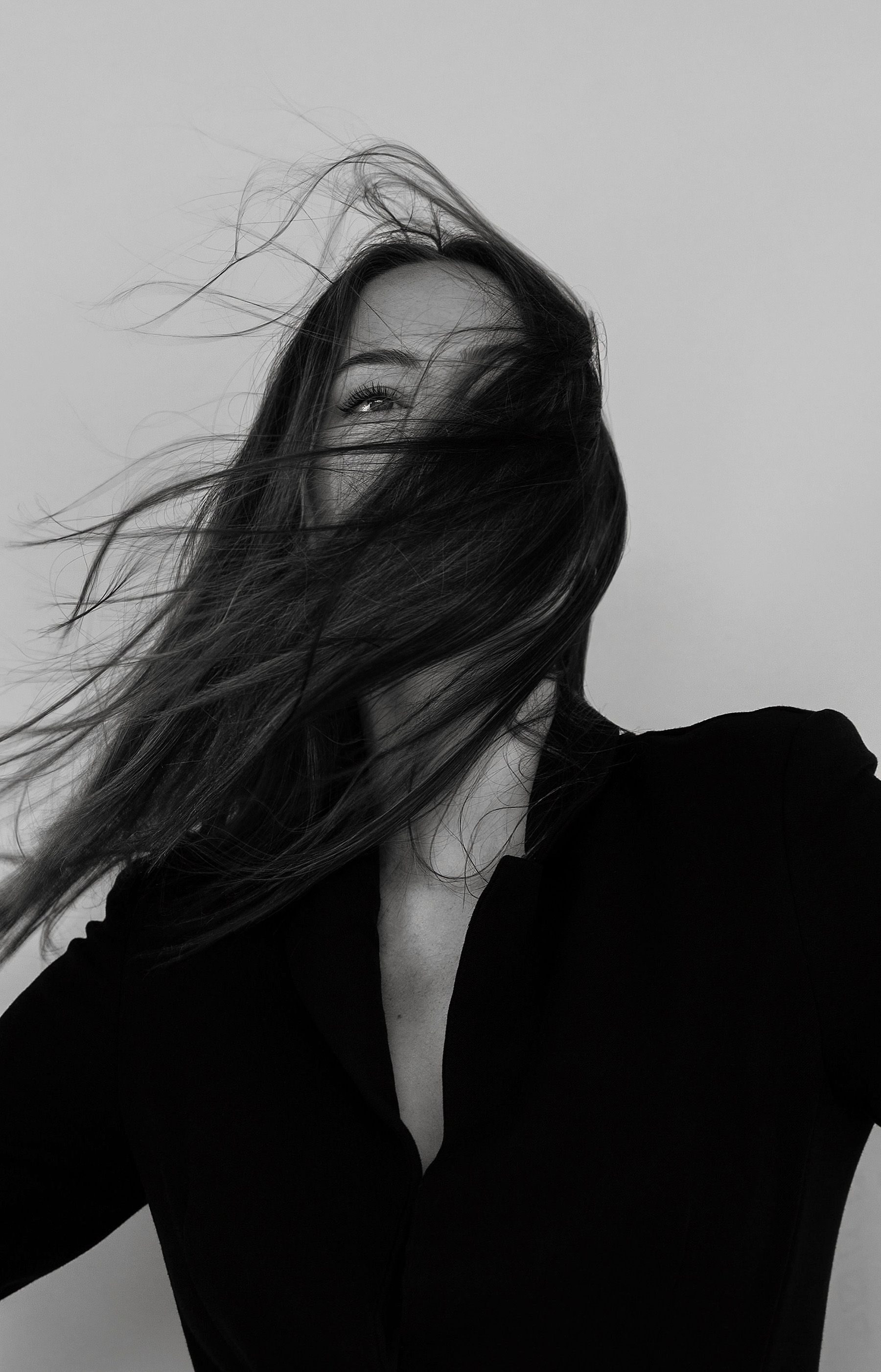 Woman with long hair blowing across her face; wearing a dark blazer.