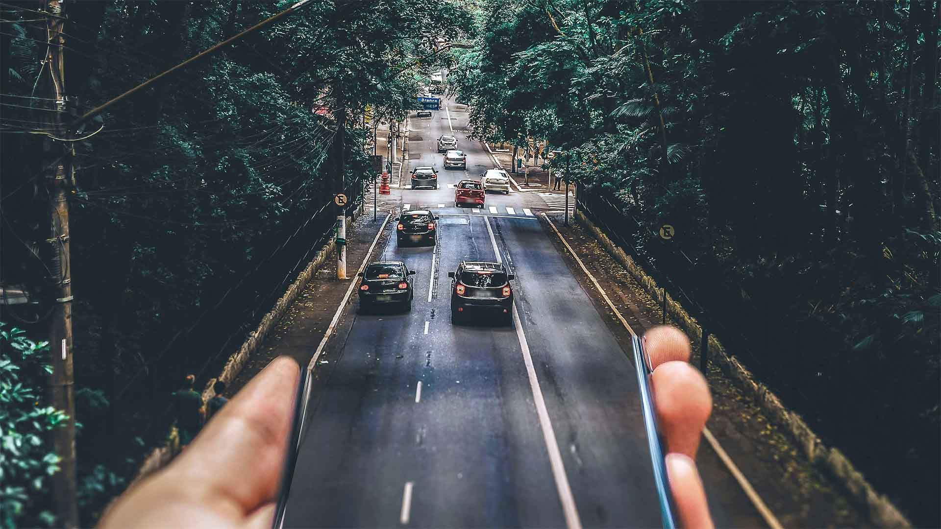 Eine Person hält ein Mobiltelefon über einer stark befahrenen Autobahn.