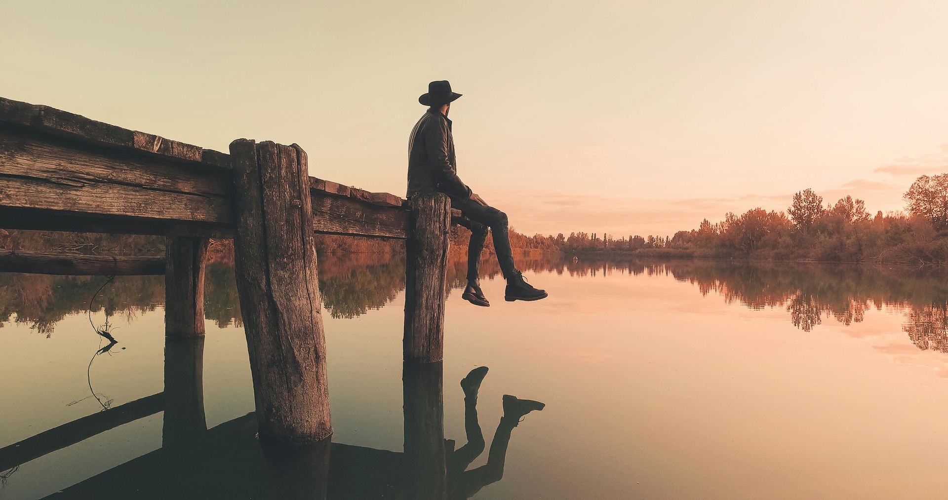 Person sitting alone on a wooden dock at sunset, reflecting on awareness and deeper soul patterns