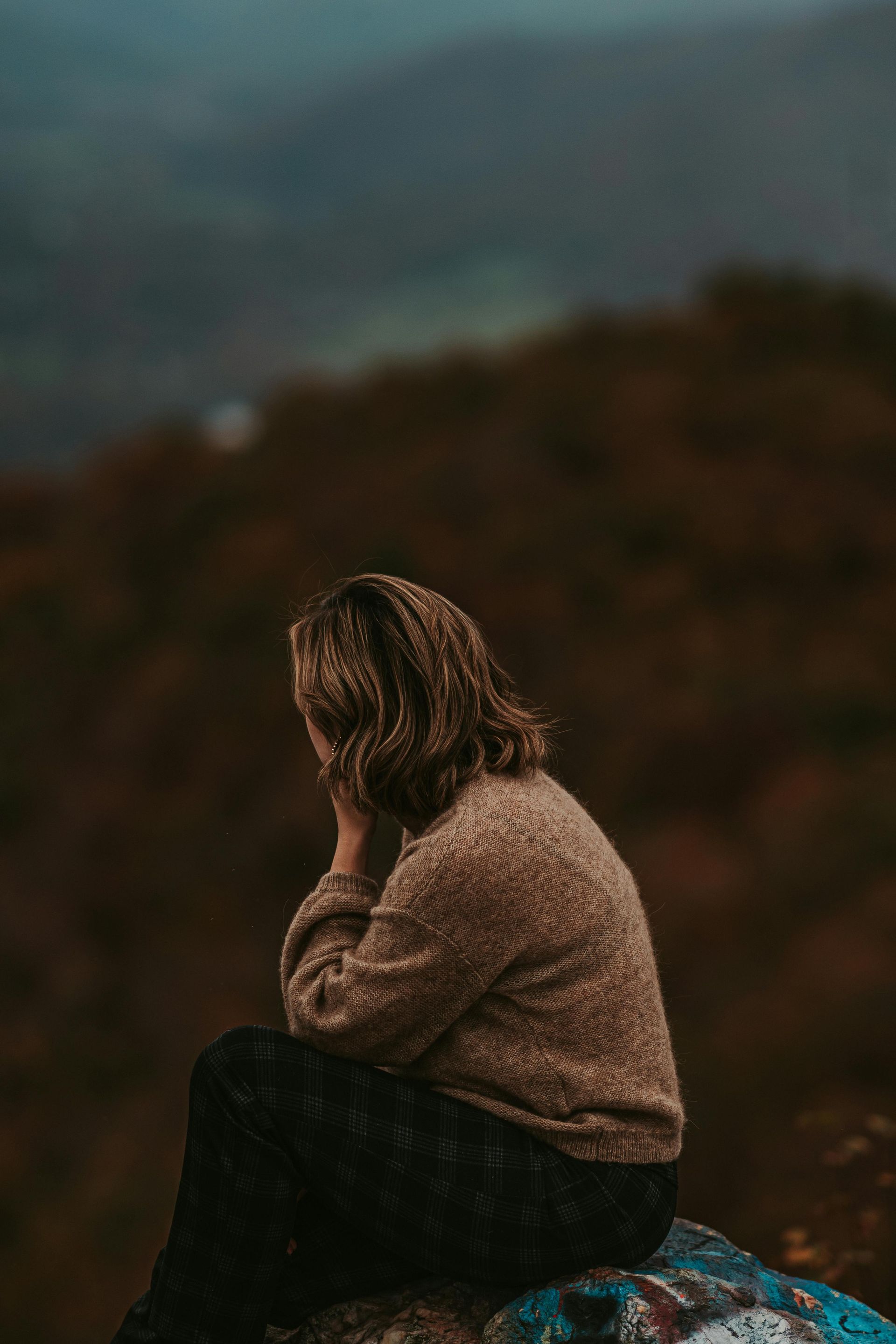 Reflective woman sitting alone in nature, symbolizing inner awareness and repeating soul lessons