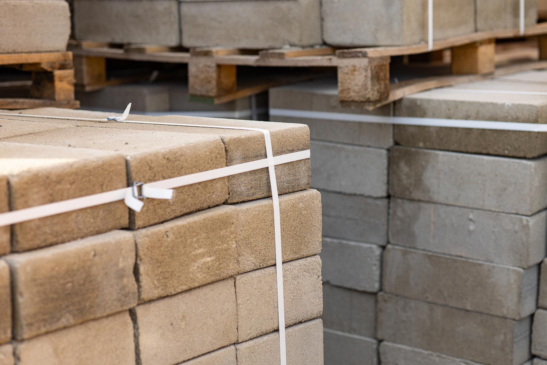 Stacks of tan and gray paving bricks on wooden pallets in a warehouse area