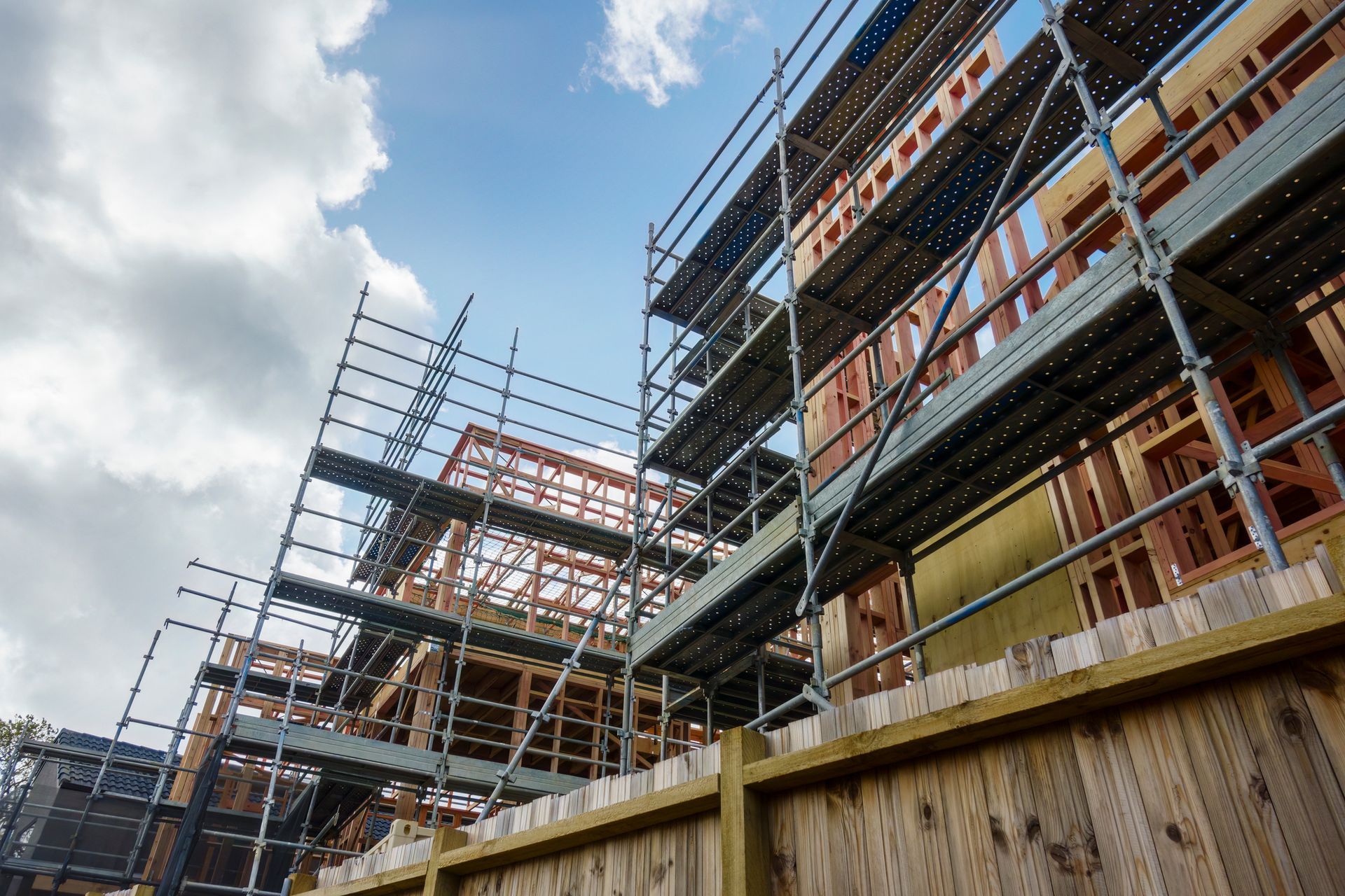 A building under construction with scaffolding and a wooden fence.