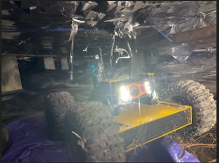 Yellow robot with large tires and headlights navigates through a dark, enclosed space, possibly a mine or tunnel.