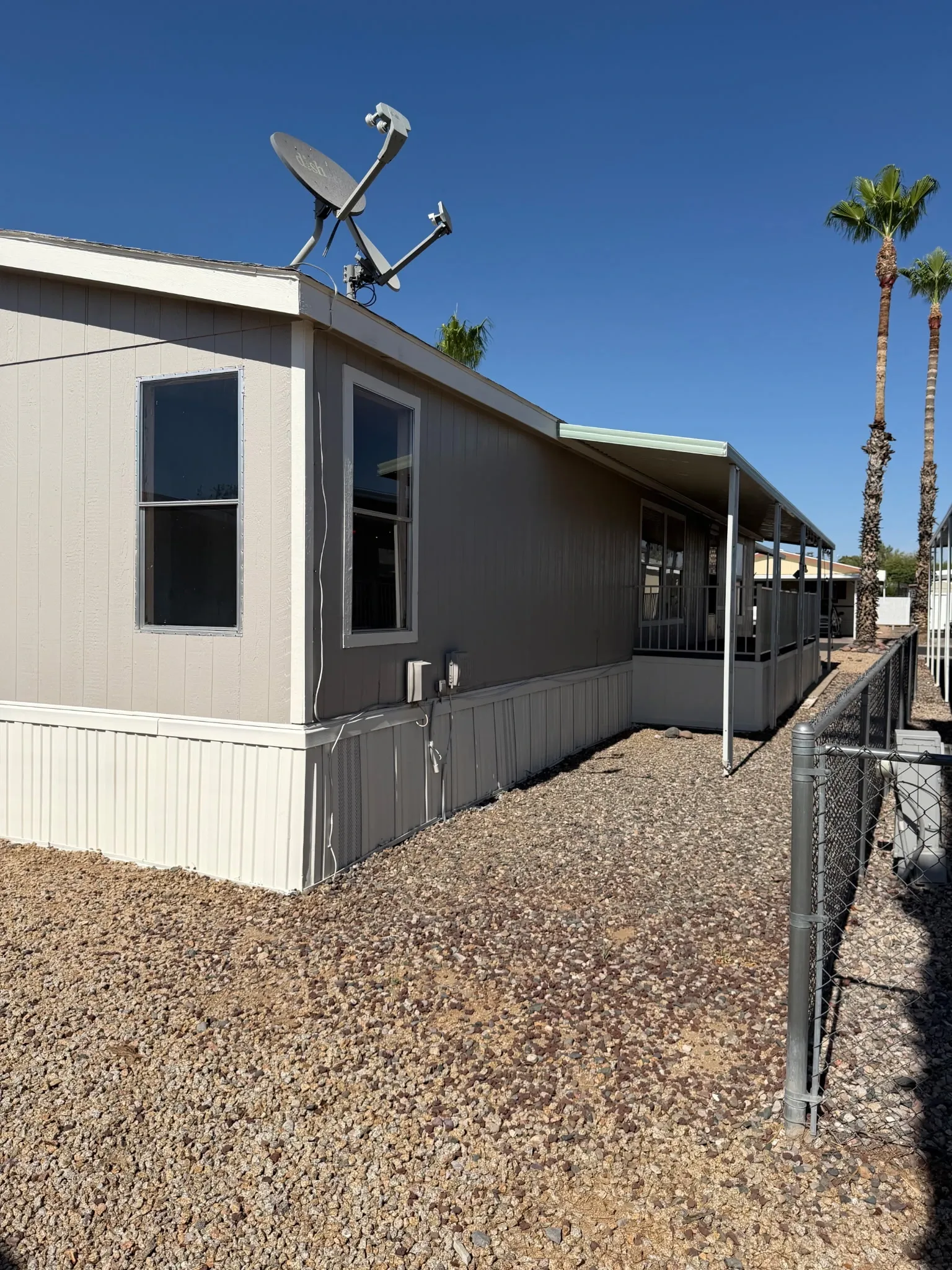 Skirted manufactured home with gravel yard and palm trees