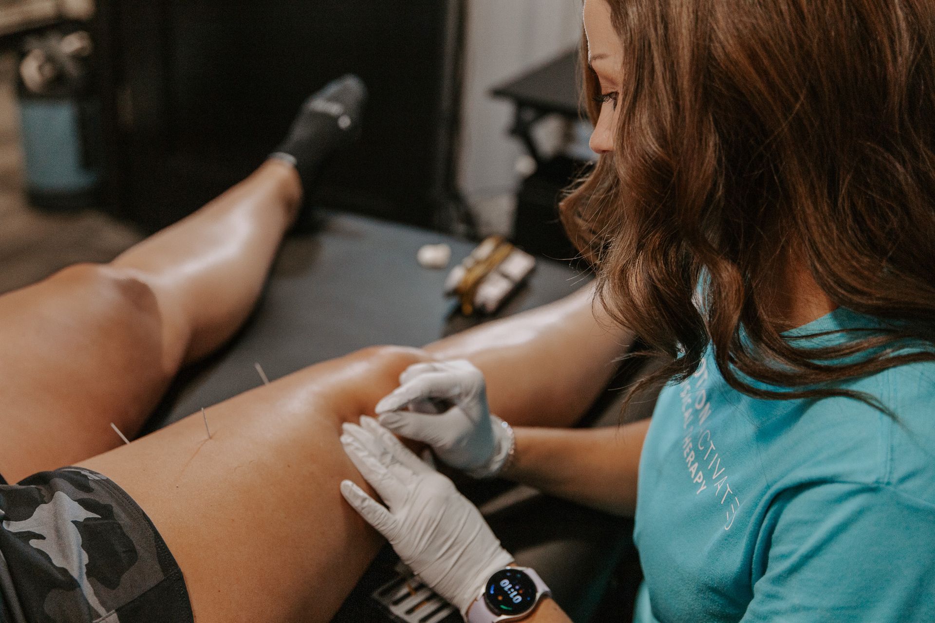 Person in teal gloves administering a treatment to a patient’s leg in a clinic setting