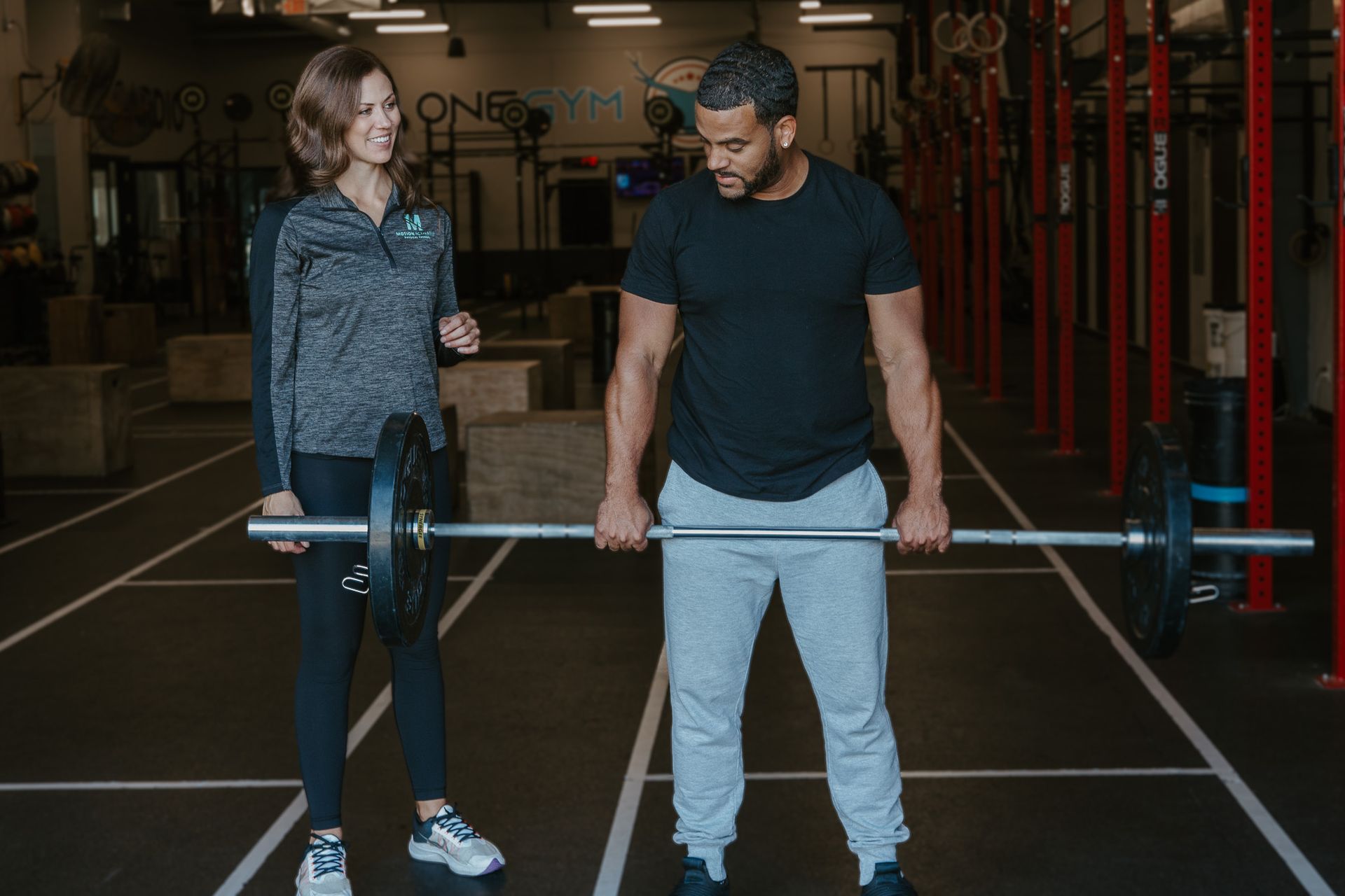 Two people holding a barbell in a gym, standing on lifting platforms.